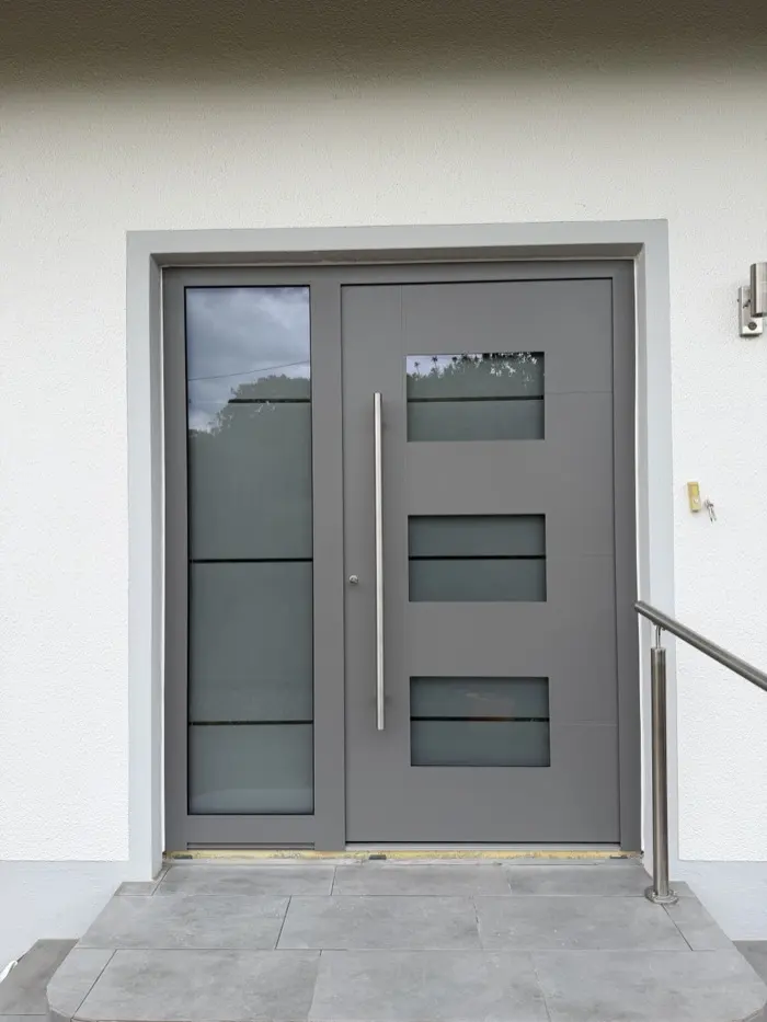 Moderne graue Haustür mit Glas-Seitenteil und Edelstahl-Stoßgriff, eingebaut von Bauelemente Ruffing
